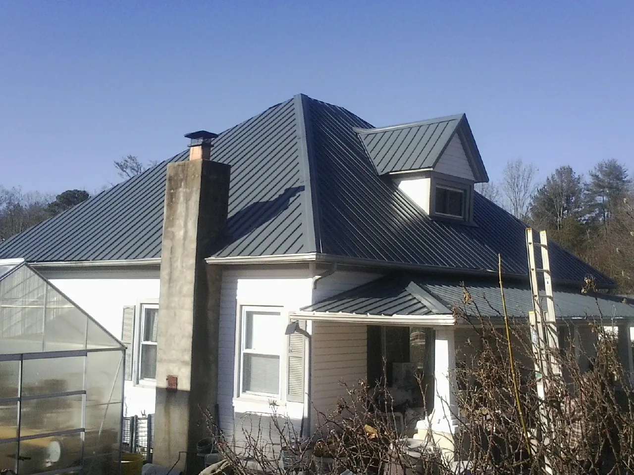 Dark blue standing seam metal roof on a white farmhouse with dormer — Slate & Tile Roof Repair by Roofing Brothers in Roxboro