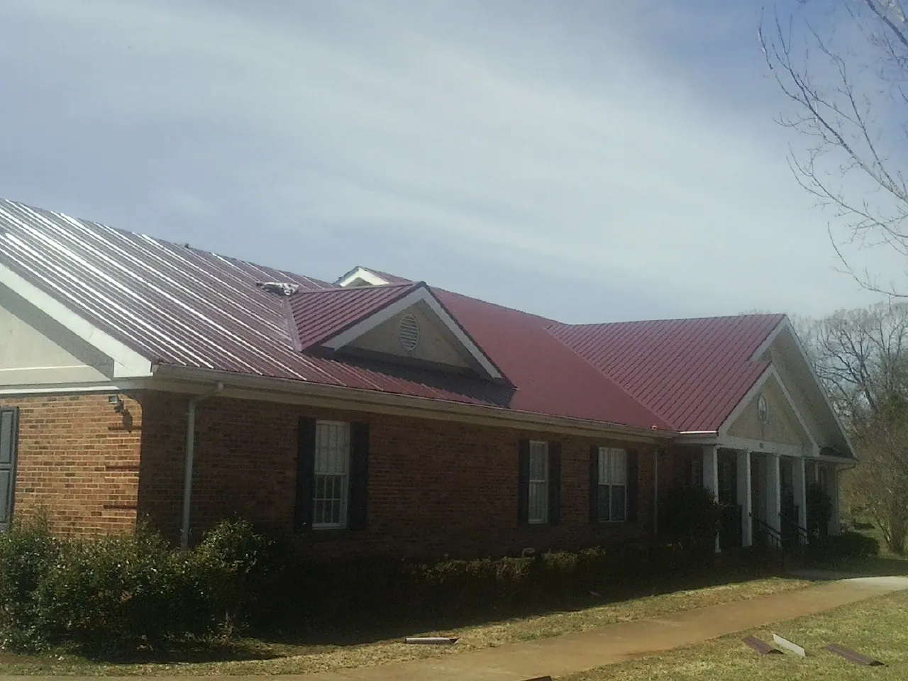 Red metal roof with gabled entries on a long brick building, from a Hail Damage Roof Repair job in Roxboro