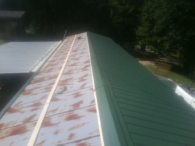 Old rusted panels beside newly installed green metal roofing — Wind Damage Roof Repair by Roofing Brothers in Roxboro