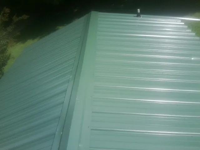 New green metal panels meeting at the ridge of a roof — Flat Roof Repair work by our crew in Roxboro