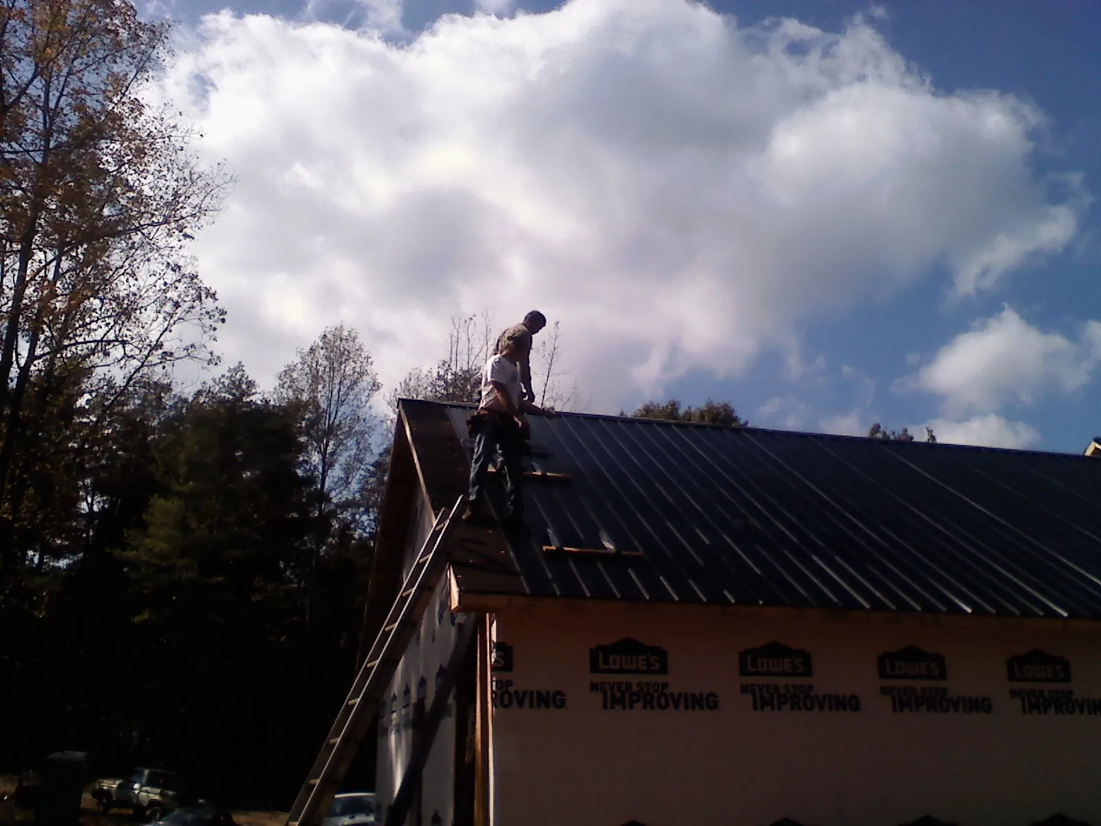 Roofer fastening dark metal panels high against a cloudy sky, from a Roof Inspection job in Roxboro