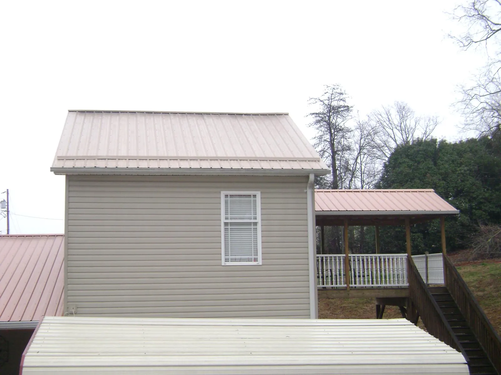 Tan metal roofs on a two story addition and attached porch, from a Roof Replacement job in Roxboro